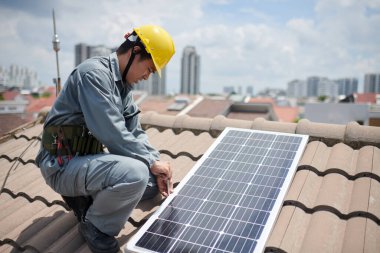 Üniformalı ve şapkalı işçiler çatıda güneş panelini vidalayacaklar.
