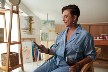 Gülümseyen olgun bir kadın şarap içiyor ve arkadaşlarına mesaj atıyor.