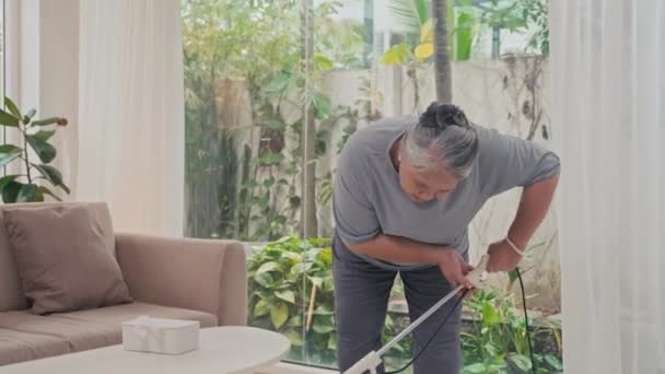 Ανώτερη Γυναίκα Κάνει Καθαρισμό Κενού Στο Σαλόνι — Αρχείο Βίντεο