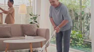 Birkaç yetişkin, oturma odasında süpürge temizliği ve toz temizleme yapıyor.