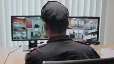 İş yerindeki CCTV kameralarına bakarken mikrofondan konuşan güvenlik görevlisinin arka görüntüsü