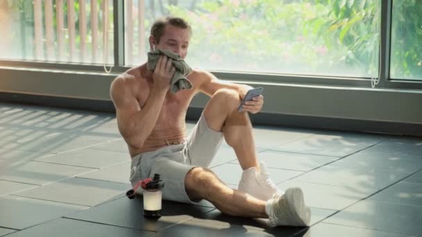 长时间坐在地板上 瓶装水 在健身房训练后在智能手机上上网的运动员 — 图库视频影像