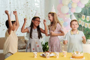 Excited kids dancing under falling confetting at birthday party clipart