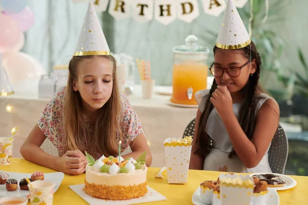 女の子でパーティー帽子吹いてキャンドルオン誕生日ケーキ — ストック写真