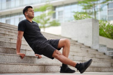 Sporcu trisepse odaklanırken kulaklıkla müzik dinliyor.