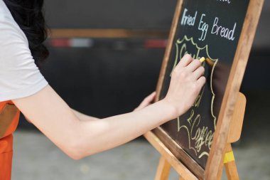 Küçük işletme sahibinin karatahtaya sokak yemekhanesi menüsü yazarken yakın plan görüntüsü.