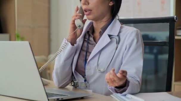 身着工作服的女性诊所经理坐在办公桌前接听病人电话的中景照片 — 图库视频影像