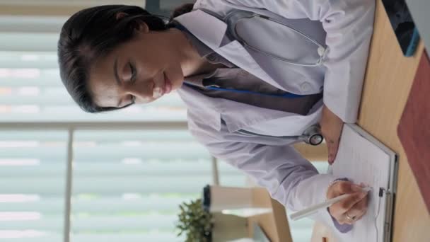女性全科医生的垂直肖像 填写病人医疗卡 在工作场所的橱柜里看着相机 — 图库视频影像