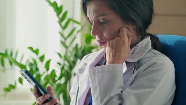 女性医生在工作休息时对智能手机上的信息感到失望的中等程度特写镜头 — 图库视频影像