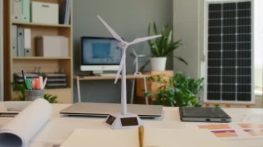 Mühendislik ofisinde arka planda bitki ve bilgisayar bulunan rüzgâr türbininin orta boy plastik görüntüsü.