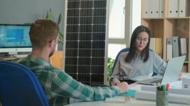 Erkek mühendis ve kadın yöneticinin, ofiste otururken özel evlerde sağladıkları güneş enerjisi projesinin detaylarını tartışırken omuz üstü çekimleri.