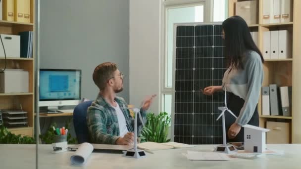 オフィスで代替エネルギープロジェクトに取り組んでいる間 男性エンジニアに新しい太陽光パネルを示す女性マネージャー — ストック動画