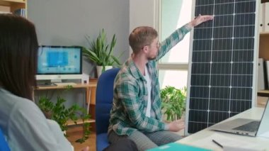 Omzundan vurulan genç mühendis, ofiste birlikte otururken panelden müşteriye güneş enerjisi projesini gösteriyor.