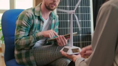 Mühendis ve yöneticinin kanat türbini modelini tutarken rüzgar enerjisi projesini tartışırken ve ofisteki dijital tablet üzerine notlar alırken görüntüsü kesildi.