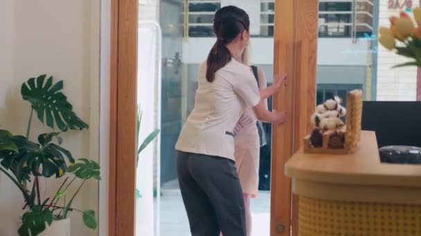 中长镜头下 年轻快乐的白人女子走进温泉沙龙 亚洲女性管理员为客人打开了大门 — 图库视频影像
