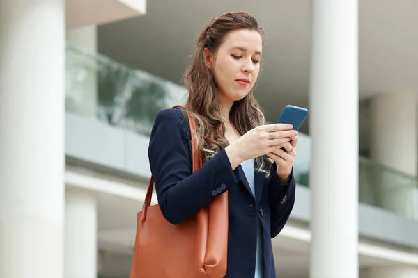 若い女性起業家立って屋外とチェックテキストメッセージ上の彼女の電話 — ストック写真