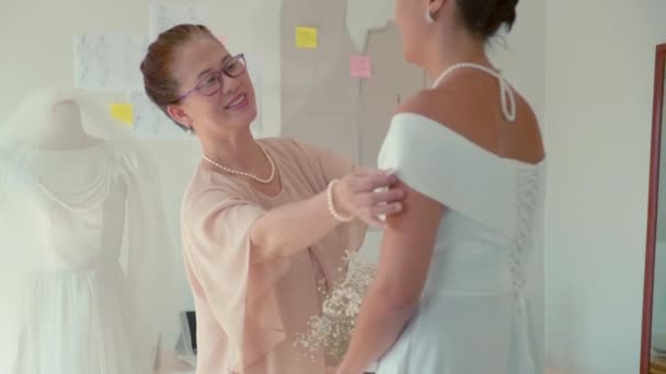 スタジオでエレガントな白いウェディングドレスで美しい娘を見ている幸せな母親のミディアムショット — ストック動画
