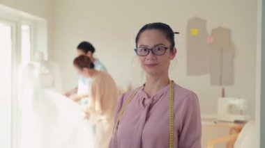 Gelin ve annesi gelinlik için kumaş seçerken fotoğrafa bakıp gülümseyen terzinin portresi.