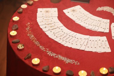 Tarot kartları, rünler ve yanan mumlar kırmızı bezle kaplı masada.