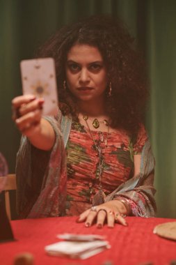 Serioius falcı tarot kartını gösteriyor ve kameraya bakıyor.