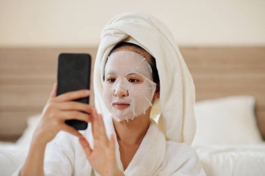 Yüzünde çarşaf maskesi olan genç bir kadın arkadaşlarına mesaj atıyor ya da sosyal medyaya bakıyor