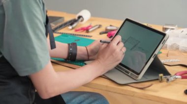 Çanta tasarımı yapan ve atölyedeki dijital tablete model çizen deri ustasının elleri orta boy yakın görünüm