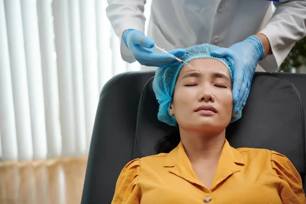 Cosmetologist injecting anti-wrinkle treatment in forehead of patient