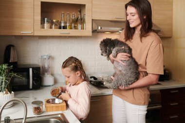 Gülümseyen bir kadın köpeğini kaldırırken ona kaseyi nasıl yiyecekle doldurduğunu gösterir.