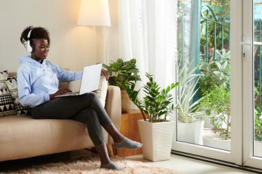 Bilgisayarında blogu için video düzenlerken kulaklık takan olumlu genç siyahi kadın