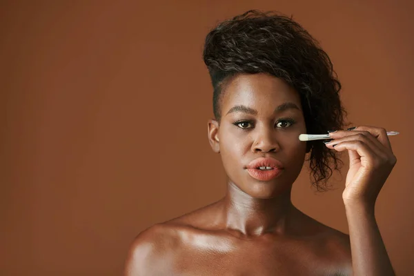 フラット合成ブラシで頬にハイライトを適用する若い黒人女性 — ストック写真