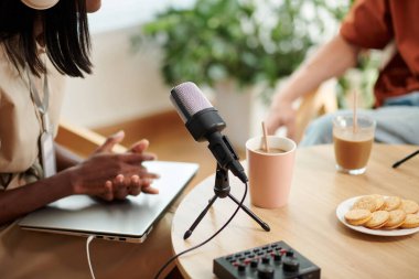 Podcaster ve masasının önündeki masada mikrofon var.