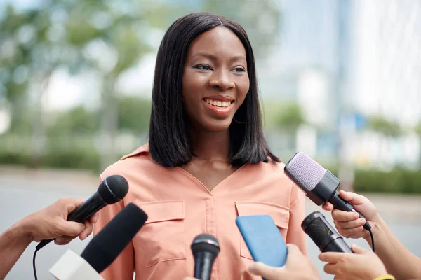 Smiling Black woman giving press conference to journalists from various media