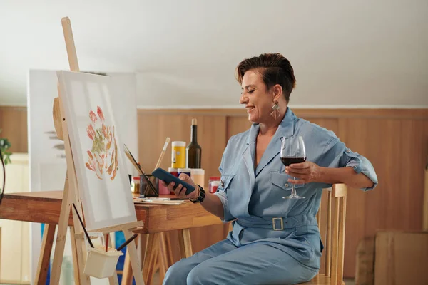 stock image Creative woman texting friend when drinking wine and painting in her studio