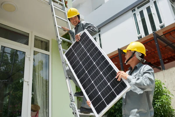 Dva Dodavatelé Montérkách Hardhats Zvedání Solární Panel Střeše — Stock fotografie
