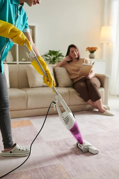 Wanita Beristirahat Sofa Dengan Buku Ketika Petugas Kebersihan Membersihkan Karpet — Stok Foto