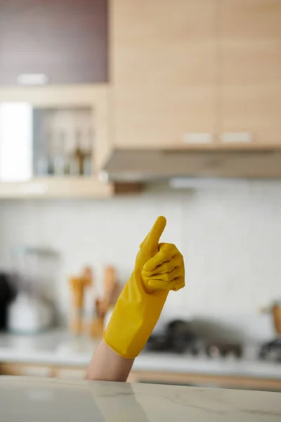 キッチンカウンターの下から親指を示す黄色いシリコーンの手袋 — ストック写真