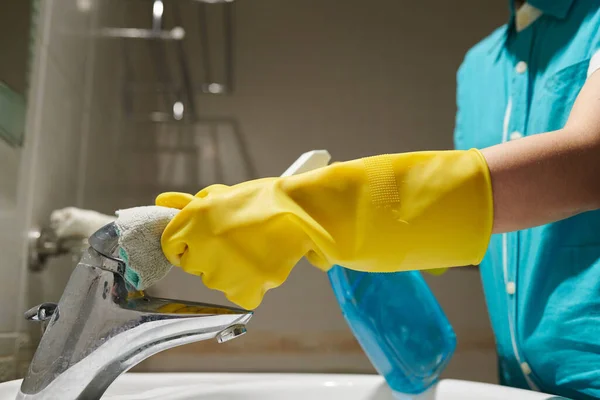 Hands of maid wearing silicone gloves when cleaning water tap in bathroom