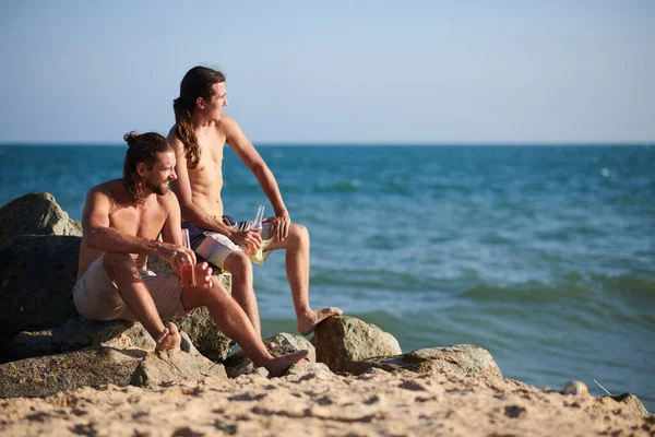 Hombres Sentados Roca Playa Bebiendo Bebidas Refrescantes Mirando Las Olas —  Fotos de Stock