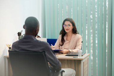 Gülümseyen insan kaynakları yöneticisi adayla konuşuyor ve panoya notlar alıyor