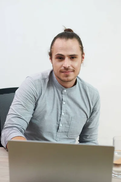 Portrait of young entrepreneur with man bun hairstyle working on laptop in office