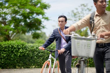 Ciddi bir Vietnamlı işadamı karşıdan karşıya geçerken bisikletinin yanında yürüyor.