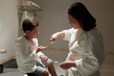 Gülümseyen anne ve oğul, akşam yatmadan önce dişlerini fırçalıyorlar.