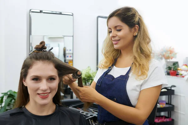 发型师用圆形刷子梳理笑脸女客户的头发 — 图库照片