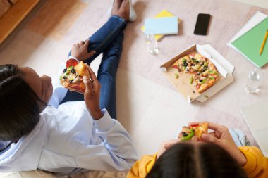 Ödevlerini bitirdikten sonra pizza yiyen genç kızlar yukarıdan bakıyorlar.