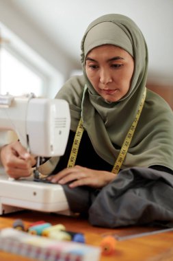 Müslüman terzi müşteri için elbise dikerken dikiş makinesi kullanıyor