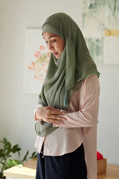 Sad pensive muslim woman in hijab praying at home