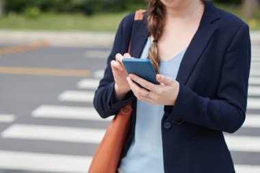 Yol kenarında duran ve iş arkadaşından gelen mesajlara cevap veren iş kadınının kırpılmış görüntüsü