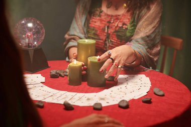 Falcının elleri masaya yanan mumlar ve yayılan tarot kartları koyuyor.