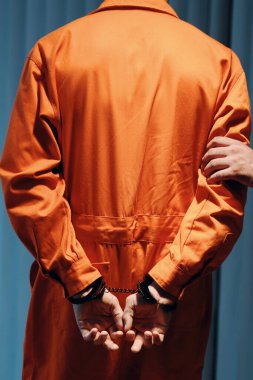 Tutuklu polis memuru turuncu üniformalı bir suçluyu hapishaneye götürüyor.