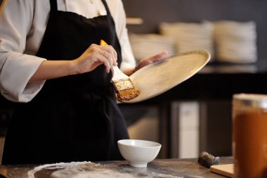 Pizzacı, tepsiyi ince bir sebze yağıyla kaplarken sentetik fırça kullanıyor.